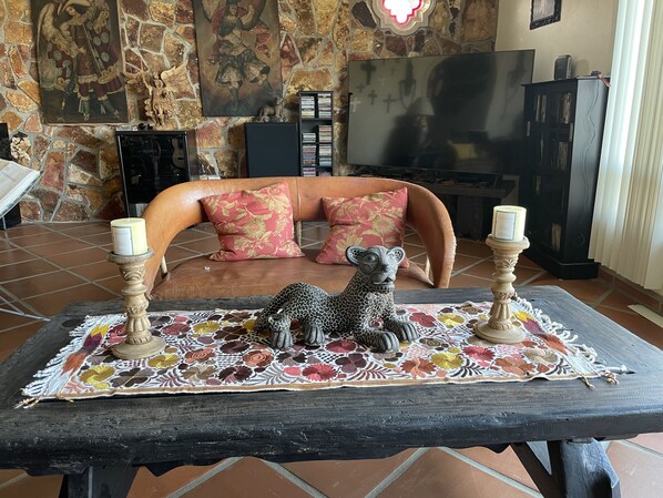 A cozy living room with a stone wall, a sofa with floral cushions, a coffee table with decorative items, and a television. - Beach Front House, Bajas getaway (Ejido Eréndira)
