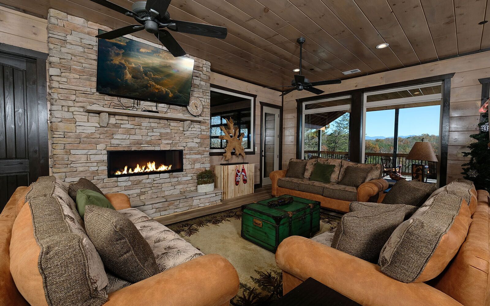 A cozy living room with a stone fireplace, leather sofas, and a large window overlooking a scenic view.