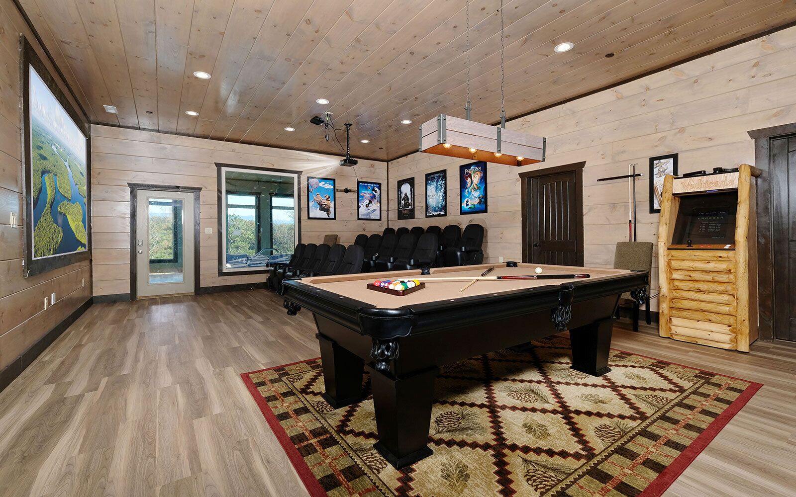 A pool table in a room with wooden walls and ceiling, a projector, and framed movie posters.