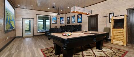 A pool table in a room with wooden walls and ceiling, a projector, and framed movie posters.