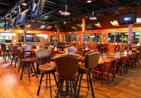 A spacious restaurant with multiple tables and chairs, large windows, and overhead lighting.
