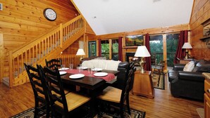 Interior de una cabaña de madera con comedor, sala de estar y una escalera.