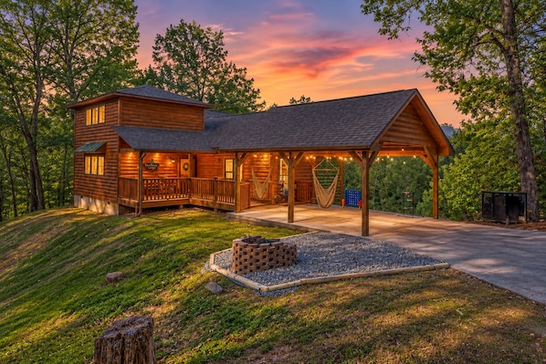 A log cabin with a covered porch and a fire pit area.