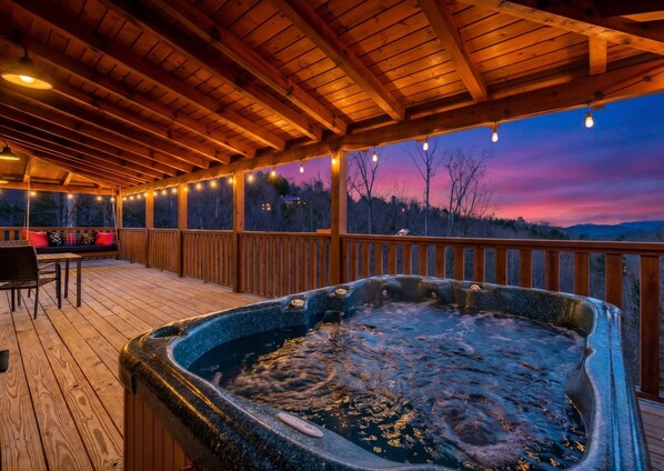 En træterrasse med jacuzzi, gyngestol og et bord med stole.