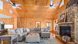 A cozy log cabin interior with a sectional sofa, a fireplace, and a ceiling fan. - Mountain VIEWS! Hot Tub, Handicap Accessible - 15 mins to downtown Gatlinburg (Sevierville)