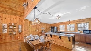 A wooden cabin-style kitchen with a dining table set for four, a refrigerator, and a large island with a sink. - Mountain VIEWS! Hot Tub, Handicap Accessible - 15 mins to downtown Gatlinburg (Sevierville)