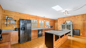 A kitchen with wooden cabinets, a black refrigerator, a dishwasher, and a granite countertop island. - Mountain VIEWS! Hot Tub, Handicap Accessible - 15 mins to downtown Gatlinburg (Sevierville)