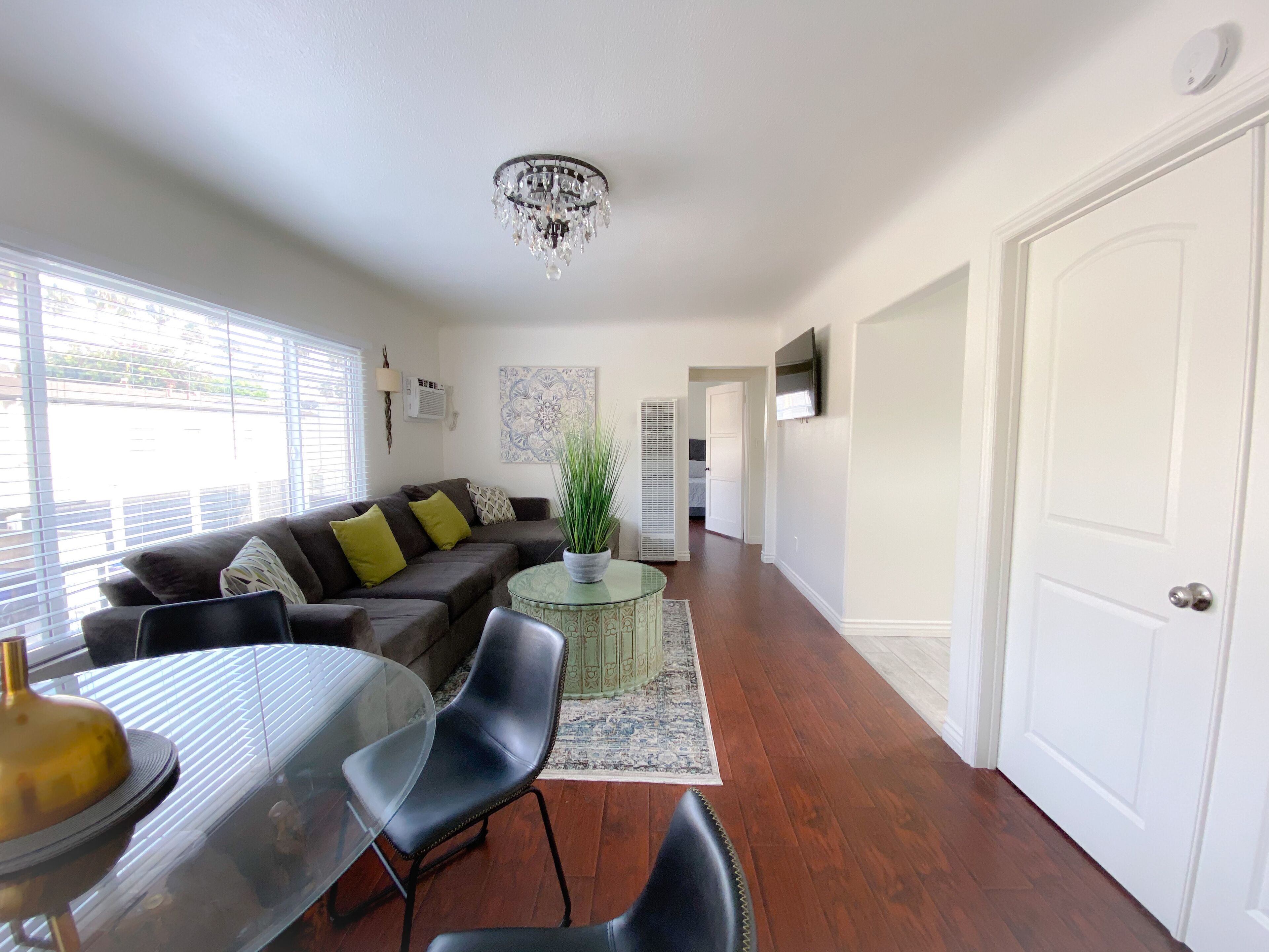 A living room with a sofa, chairs, a glass table, a chandelier, and a door.