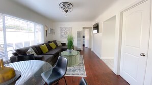 A living room with a sofa, chairs, a glass table, a chandelier, and a door.