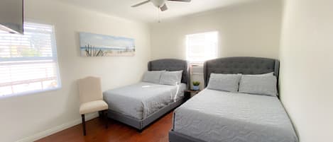 A bedroom with two beds, a ceiling fan, a painting on the wall, and a window with blinds.