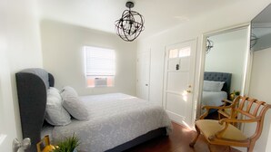 A bedroom with a bed, a chair, a mirror, and a chandelier.