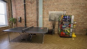 Una mesa de ping pong en una habitación con pared de ladrillo y una máquina expendedora que ofrece aperitivos y bebidas.