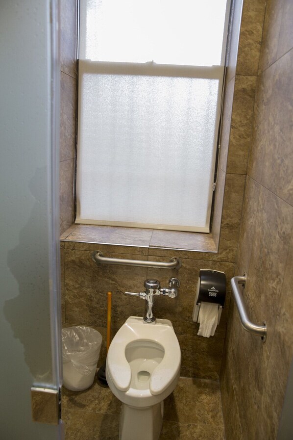 A small bathroom with a toilet, a handrail, and a window.