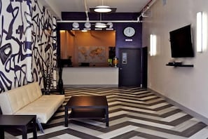 A modern lobby with a sofa, a coffee table, a reception desk, a world map, clocks, and a TV. - B Hotel and Hostel (Brooklyn)