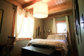 A cozy bedroom with a wooden ceiling, a bed with a plaid bedspread, a nightstand, and a chair.