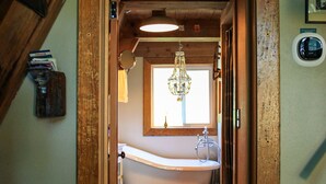 Un pasillo estrecho que conduce a un baño con bañera, ventana y techo de madera.
