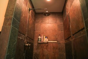 A shower with a handheld showerhead, a shelf with toiletries, and a door with a handle.