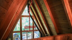 Un dormitorio abuhardillado de madera con techo inclinado, una ventana con estante de metal y vistas al exterior.
