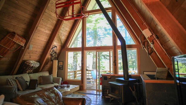 Un cuarto ático acogedor con techo de madera, un ventanal grande, chimenea y un sofá.
