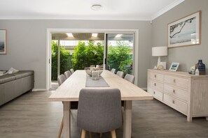 Enjoy meals in this spacious dining area with a long table, sofa, and large window offering a view of lush greenery.
