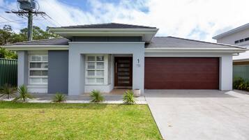 A modern two-story house with a garage, a front porch with a bench, and a well-maintained lawn.