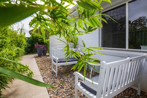 Relax in a serene outdoor space with a bench and chair, surrounded by lush greenery and a gravel path.