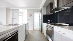 A modern kitchen with white cabinetry, stainless steel appliances, and a central island. - Callala Bay Beach House - Wowly Waters - Pet Friendly   🐳 (Callala Bay)