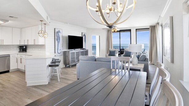 A modern living room with a dining area, a kitchen, and a balcony with a view. - Beachfront 3BR @ Phoenix X • Sleeps 10 • Gulf Views • Next to Flora-Bama & Resort Amenities (Orange Beach)