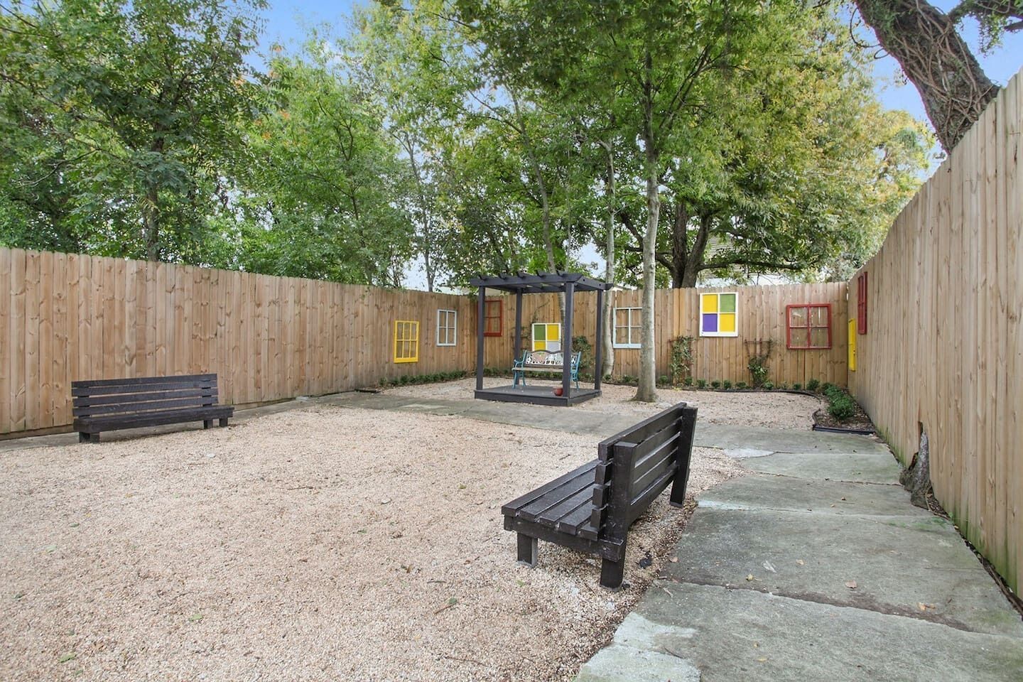 A fenced backyard with two wooden benches, a covered seating area, and a gravel path.