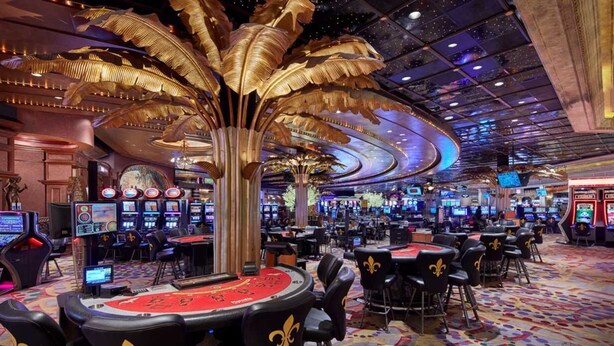Un casino con múltiples mesas de juego, una gran escultura de una palmera dorada y una alfombra vibrante y con diseños.
