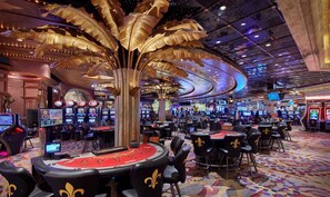 Ein Casino mit mehreren Spieltischen, einer großen Skulptur einer goldenen Palme und einem farbenfrohen, gemusterten Teppich.