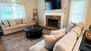 A living room with a fireplace, a sofa set, a coffee table, and a TV mounted above the fireplace.