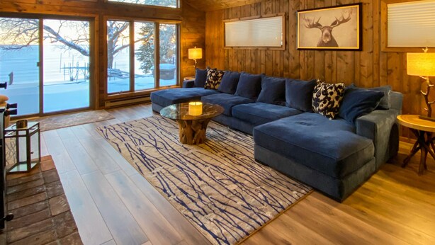 Ein geräumiges Wohnzimmer mit einem großen Ecksofa, einem Deckenventilator aus Holz und einem großen Fenster mit Blick ins Freie.
