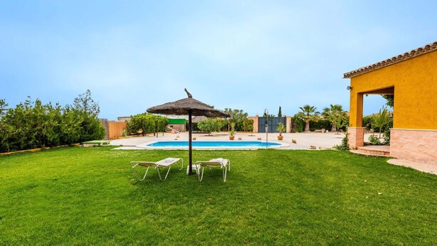 Un jardin avec une piscine, un espace salon couvert et un bâtiment jaune.