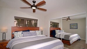 Une chambre à coucher avec un grand lit, un ventilateur de plafond, un miroir et une table de chevet avec une lampe.