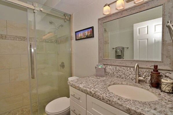 A bathroom with a glass shower enclosure, a sink with a marble countertop, and a large mirror above the sink. - Newly remodeled ocean view condo - Kihei Alii Kai (Kihei)
