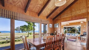 A wooden interior with a dining area, large windows, and a view of the sea.