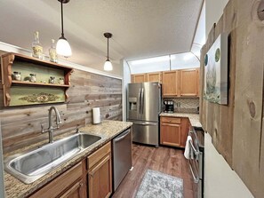 A compact kitchen with wooden cabinets, a stainless steel refrigerator, and a granite countertop. - CQS 26 Catalonia Ct Conquistador (St. Augustine)