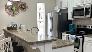 A kitchen with white cabinetry, a stainless steel refrigerator, a microwave, a stove, and a trash can. - Condo super close to the beach with a view of SpaceX Launch in the sky! (south padre island)