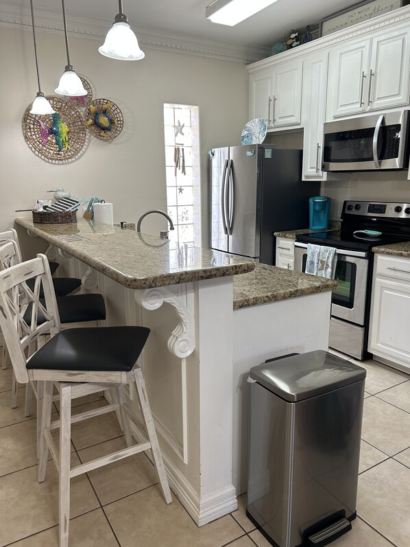 A kitchen with white cabinetry, a stainless steel refrigerator, a microwave, a stove, and a trash can.