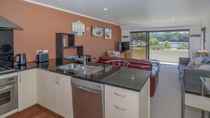 Una cocina moderna con lavavajillas, estufa y lavabo. Hay un comedor con un sofá rojo y vistas al exterior.