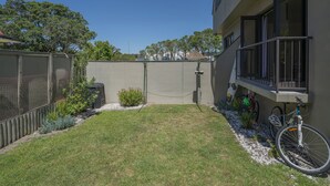 Un patio trasero residencial con área cercada, un pequeño jardín y una bicicleta apoyada en la edificación.