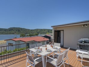 Een balkon met een eettafel, met uitzicht op een waterpartij en een bebost heuvel.