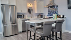 Une cuisine moderne dotée d’appareils électroménagers en acier inoxydable, d’un îlot central avec des tabourets de bar et d’un pare-feu orné de motifs en mosaïque.