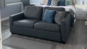 Une chambre à coucher avec un lit, un canapé gris, un ventilateur de plafond et une fenêtre avec des rideaux.