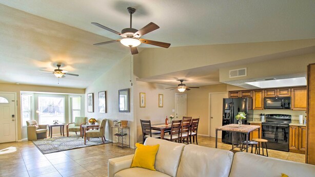 A spacious living area with a beige leather sofa, dining table, and chairs, a kitchen with wooden cabinets and appliances, and two ceiling fans. - Near Golf & Entertainment! Gilbert Family Getaway (Gilbert)