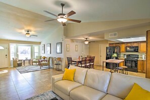 A spacious living area with a beige leather sofa, dining table, and chairs, a kitchen with wooden cabinets and appliances, and two ceiling fans. - Near Golf & Entertainment! Gilbert Family Getaway (Gilbert)