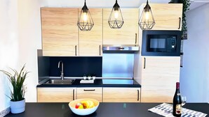 A modern kitchen with wooden cabinets, a black countertop, a stainless steel stove, and pendant lights.