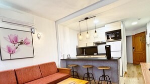 A compact living space with a sofa, a wooden table, and a kitchen area with a bar stool.