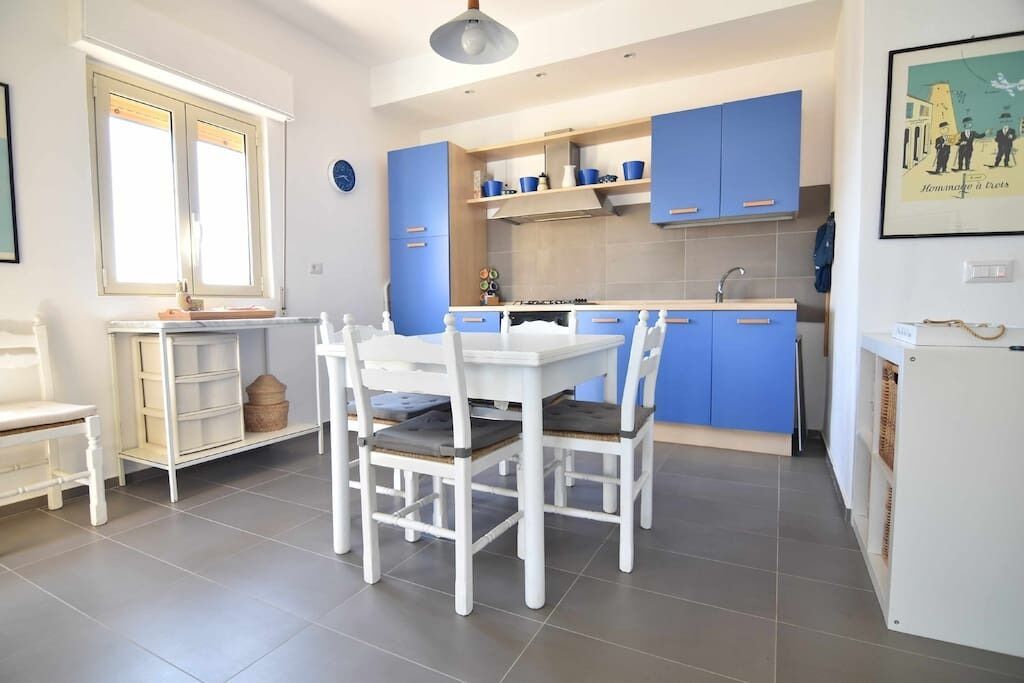 A modern kitchen with blue cabinets, a white dining table, and chairs.